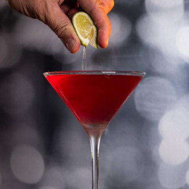Kozmopolit Kokteylinin içine dramatik ışıklandırmayla taze limon sıkıştıran parmaklar.