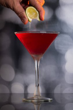Kozmopolit Kokteylinin içine dramatik ışıklandırmayla taze limon sıkıştıran parmaklar.
