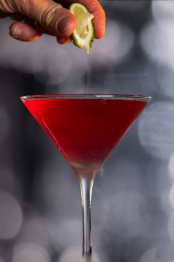 Kozmopolit Kokteylinin içine dramatik ışıklandırmayla taze limon sıkıştıran parmaklar.