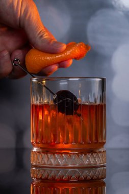 Kayalarda servis edilen viski kokteyli portakal kabuğu ve kirazla süslenmiş ve ahşap bir yüzeyde sunulan dramatik ışıklandırmayla servis ediliyor..