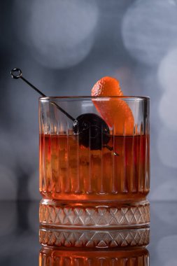Kayalarda servis edilen viski kokteyli portakal kabuğu ve kirazla süslenmiş ve ahşap bir yüzeyde sunulan dramatik ışıklandırmayla servis ediliyor..