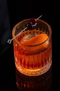 Kayalarda servis edilen viski kokteyli portakal kabuğu ve kirazla süslenmiş ve ahşap bir yüzeyde sunulan dramatik ışıklandırmayla servis ediliyor..