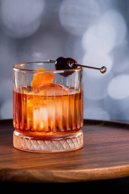 Kayalarda servis edilen viski kokteyli portakal kabuğu ve kirazla süslenmiş ve ahşap bir yüzeyde sunulan dramatik ışıklandırmayla servis ediliyor..