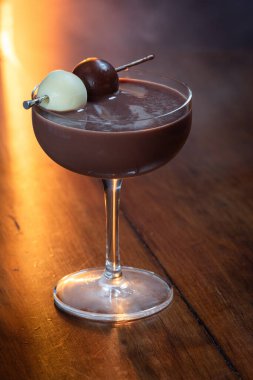 Siyah ve beyaz trüf mantarlarıyla süslenmiş, atmosferik duman ve sıcak, kırsal ahşap bir yüzey üzerinde parlayan ışık içeren zengin bir çikolata kokteylinin profesyonel yan profil çekimi..