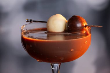 Çikolata karışımının yakın plan bir profili coupe bardakta, gümüş bir kazmada siyah ve beyaz bir çikolata mantarı ile süslenmiş, yumuşak, profesyonel bir bokeh arka planda..