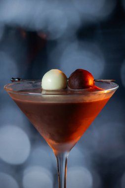 Çikolata karışımının yakın plan bir profili coupe bardakta, gümüş bir kazmada siyah ve beyaz bir çikolata mantarı ile süslenmiş, yumuşak, profesyonel bir bokeh arka planda..