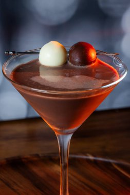 Çikolata karışımının yakın plan bir profili coupe bardakta, gümüş bir kazmada siyah ve beyaz bir çikolata mantarı ile süslenmiş, yumuşak, profesyonel bir bokeh arka planda..