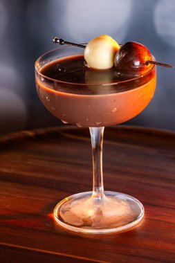 Çikolata karışımının yakın plan bir profili coupe bardakta, gümüş bir kazmada siyah ve beyaz bir çikolata mantarı ile süslenmiş, yumuşak, profesyonel bir bokeh arka planda..