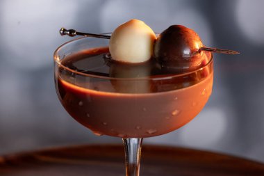 Çikolata karışımının yakın plan bir profili coupe bardakta, gümüş bir kazmada siyah ve beyaz bir çikolata mantarı ile süslenmiş, yumuşak, profesyonel bir bokeh arka planda..