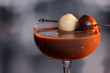 Çikolata karışımının yakın plan bir profili coupe bardakta, gümüş bir kazmada siyah ve beyaz bir çikolata mantarı ile süslenmiş, yumuşak, profesyonel bir bokeh arka planda..