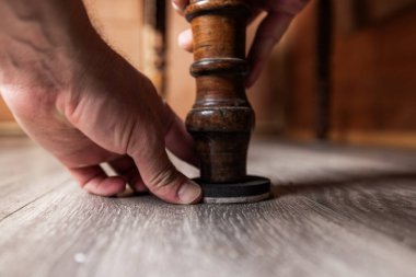 Dekoratif ahşap bir sandalyenin tabanına veya masa bacağına dairesel bir keçeli mobilya sürgüsü takan insanların detaylı bir görüntüsü. Görüntü, ev bakımını ve sert ahşabın korunmasını veya döşemeyi hasar ve aşınmalardan korumayı ön plana çıkarıyor.