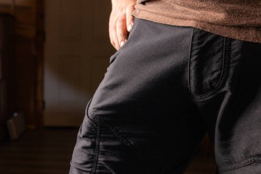 Yüksek kontrastlı mizah, siyah desenli pantolon giyen birinin yakın çekim görüntüsü, cep alanındaki farklı bir çıkıntıya ve şekle odaklanıyor.