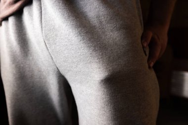 Cebinde komik bir nesne. Açık gri kumaş pantolon giyen, göze çarpan bir şekle odaklanan ve cebin içinde koyu bir arka plana doğru şişen bir kişinin detaylı görüntüsü..
