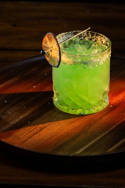 Tuzlu buzlu parlak yeşil Margarita ve dramatik ışıklandırmalı susuz limon tekeri.