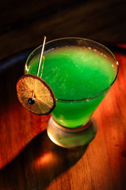 Yenebilir yeşil parıltı, yüksek anahtar ışığı ve gölgelerle aydınlatılmış ahşap bir yüzeydeki içeceği süslerdi.