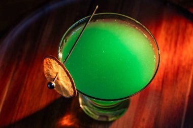 Yenebilir yeşil parıltı, yüksek anahtar ışığı ve gölgelerle aydınlatılmış ahşap bir yüzeydeki içeceği süslerdi.