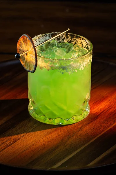 Tuzlu buzlu parlak yeşil Margarita ve dramatik ışıklandırmalı susuz limon tekeri.