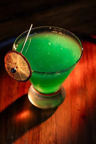 Yenebilir yeşil parıltı, yüksek anahtar ışığı ve gölgelerle aydınlatılmış ahşap bir yüzeydeki içeceği süslerdi.