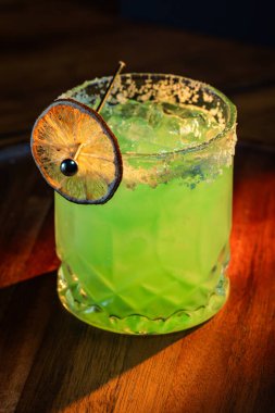 Tuzlu buzlu parlak yeşil Margarita ve dramatik ışıklandırmalı susuz limon tekeri.