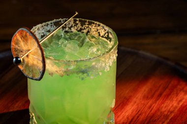 Tuzlu buzlu parlak yeşil Margarita ve dramatik ışıklandırmalı susuz limon tekeri.