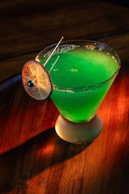 Yenebilir yeşil parıltı, yüksek anahtar ışığı ve gölgelerle aydınlatılmış ahşap bir yüzeydeki içeceği süslerdi.