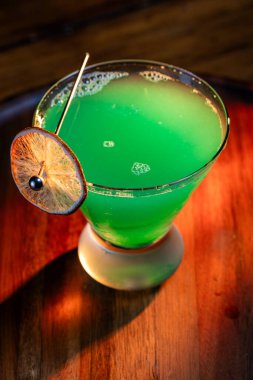 Yenebilir yeşil parıltı, yüksek anahtar ışığı ve gölgelerle aydınlatılmış ahşap bir yüzeydeki içeceği süslerdi.
