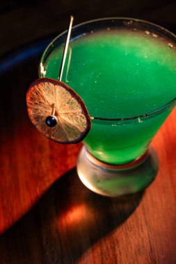 Yenebilir yeşil parıltı, yüksek anahtar ışığı ve gölgelerle aydınlatılmış ahşap bir yüzeydeki içeceği süslerdi.