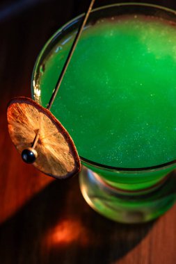 Yenebilir yeşil parıltı, yüksek anahtar ışığı ve gölgelerle aydınlatılmış ahşap bir yüzeydeki içeceği süslerdi.