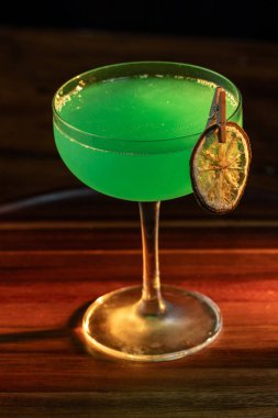 Yenebilir yeşil parıltı, yüksek anahtar ışığı ve gölgelerle aydınlatılmış ahşap bir yüzeydeki içeceği süslerdi.