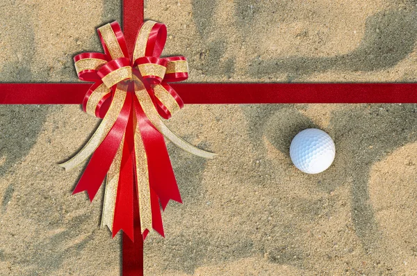 Красная лента на мяче для гольфа на песке на заднем плане — стоковое фото