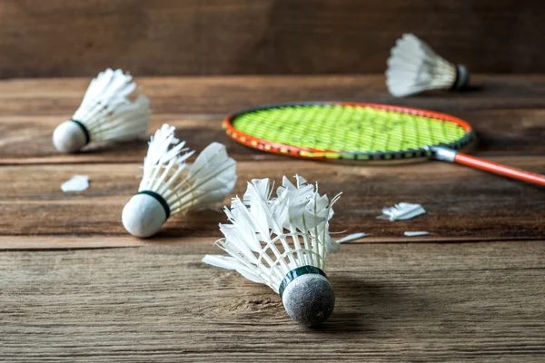 Shuttlecock and Racket with parts of its feathers scattered on wooden — Stock Photo, Image