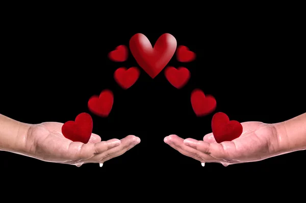 Rote Herzen fliegen auf schwarzem Hintergrund in die Hände. Liebeskonzept — Stockfoto