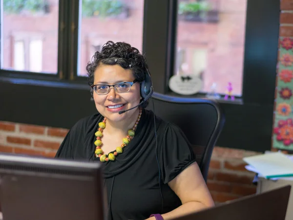 中年のヘッドフォンを身に着けているオフィス環境でヒスパニック系の女性 — ストック写真
