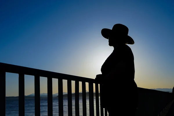 Frau mit Sonnenhut steht an Geländer Silhouette — Stockfoto