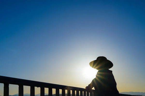 Frau mit Sonnenhut steht an Geländer Silhouette — Stockfoto