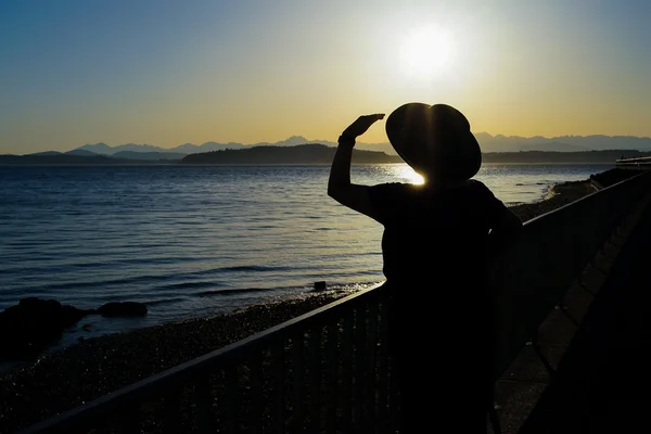 Жінка в сонячному капелюсі стоїть за рейками силует — стокове фото