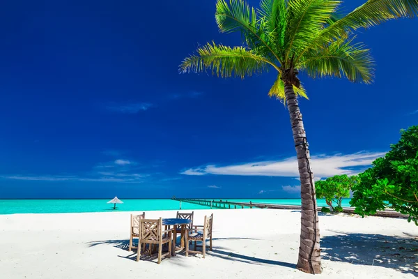 Mesas y sillas a la sombra de la palmera en un islán tropical — Foto de Stock