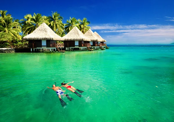 Couple snorkling in lagoon with over water bungalows — Stock Photo, Image