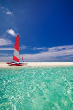 Sailing boat with red sail on beach of tropical island clipart