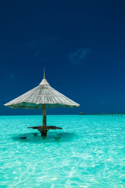 Bamboo beach umbrella with bar seats in the water of an island — Stock Photo, Image