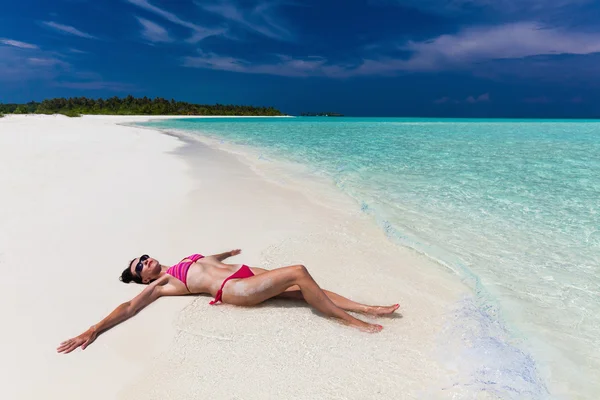 Vrouw in paars en rode bikini op het strand uitgerekt — Stockfoto