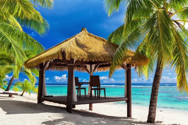 Tropical gazebo and two chairs on an island beach with palm tree Stock Image