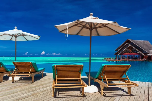 Sillas de cubierta con sombrilla con vistas a la piscina infinita y tropical —  Fotos de Stock