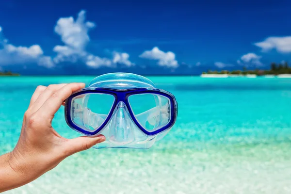 Hand met snorkel googles tegen wazig strand — Stockfoto