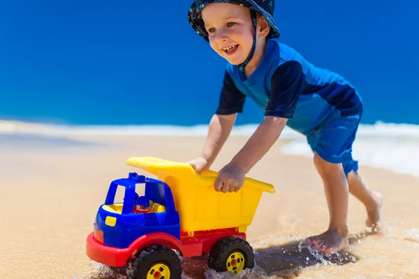 Menino empurrando carro colorido na praia — Fotografia de Stock