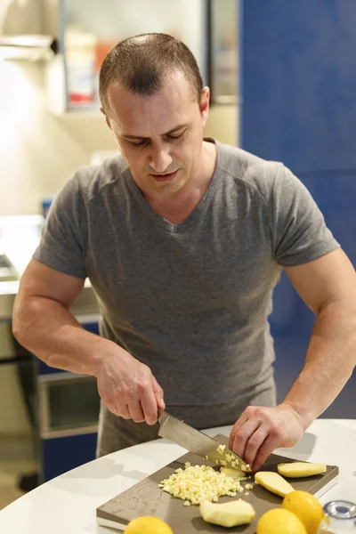 Un homme est dans sa cuisine et coupe des légumes pour préparer un — Photo