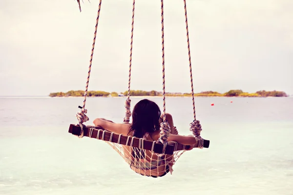 A beautiful girl in a swing on a beach in resort — Stock Photo, Image