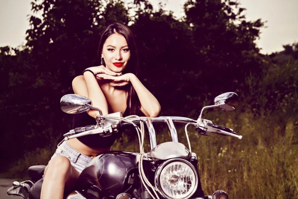Beautiful young woman posing with a motorcycle — Stock Photo, Image