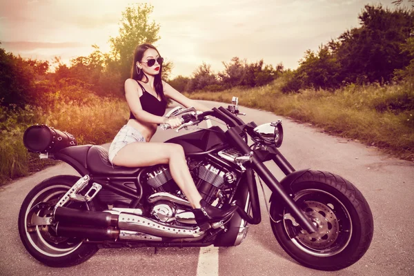 Güzel genç bir kadın motosikletle poz veriyor.