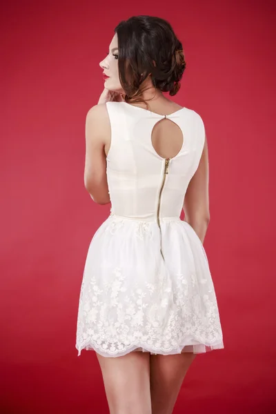 Jovem modelo feminino bonito em vestido branco no fundo vermelho — Fotografia de Stock